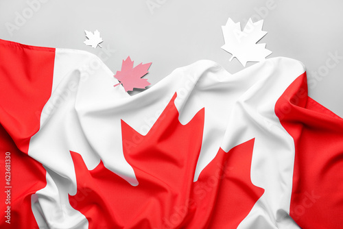 Flag of Canada and paper maple leaves on grey background