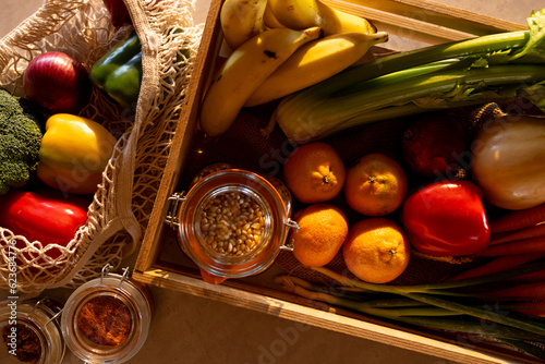 Fresh vegetables, fruit and grains in crate and re-usable shopping bag on counter in sunny kitchen photo