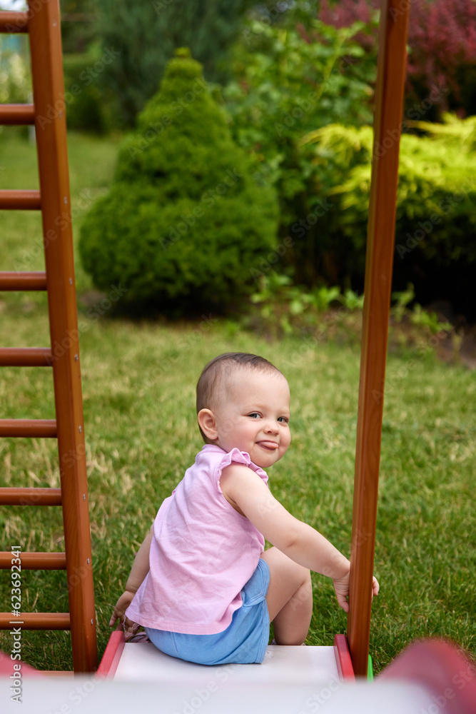baby girl playing slider in playground in summer