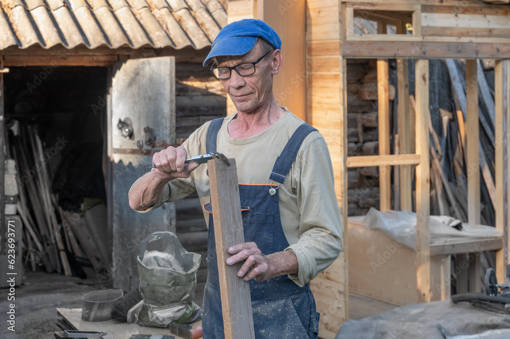 carpenter processes wooden planks while on the street on a country plot using an electric woodworking machine carpenter processes wooden planks while on the street on a country plot using an electric woodworking machine