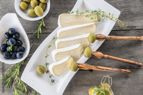 brie cheese and olives with thyme on a wooden background. Pieces of cheese on a cheese plate photo