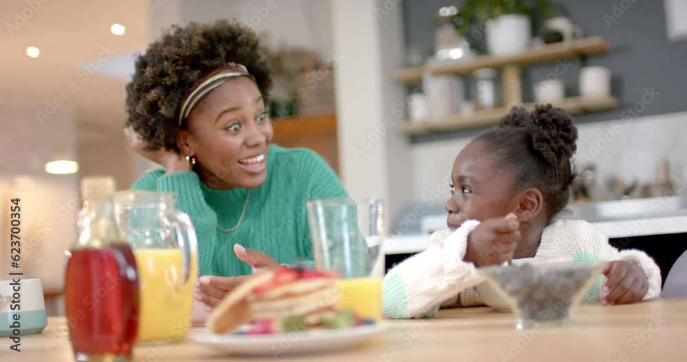 Happy african american mother and daughter eating cereal with milk in kitchen, slow motion Happy african american mother and daughter eating cereal with milk in kitchen, slow motion