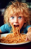 A cute greedy child is stuffing himself with a plate of pasta and smears his face and hands with sauce
