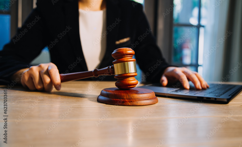 Justice and law concept.Male judge in a courtroom with the gavel, working with, computer and docking keyboard, eyeglasses, on table in morning light Justice and law concept.Male judge in a courtroom with the gavel, working with, computer and docking keyboard, eyeglasses, on table in morning light