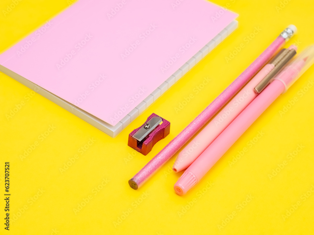 Pink office work concept, pencils, pens, markers, sharpener and notepad on a yellow background. Pink office work concept, pencils, pens, markers, sharpener and notepad on a yellow background.