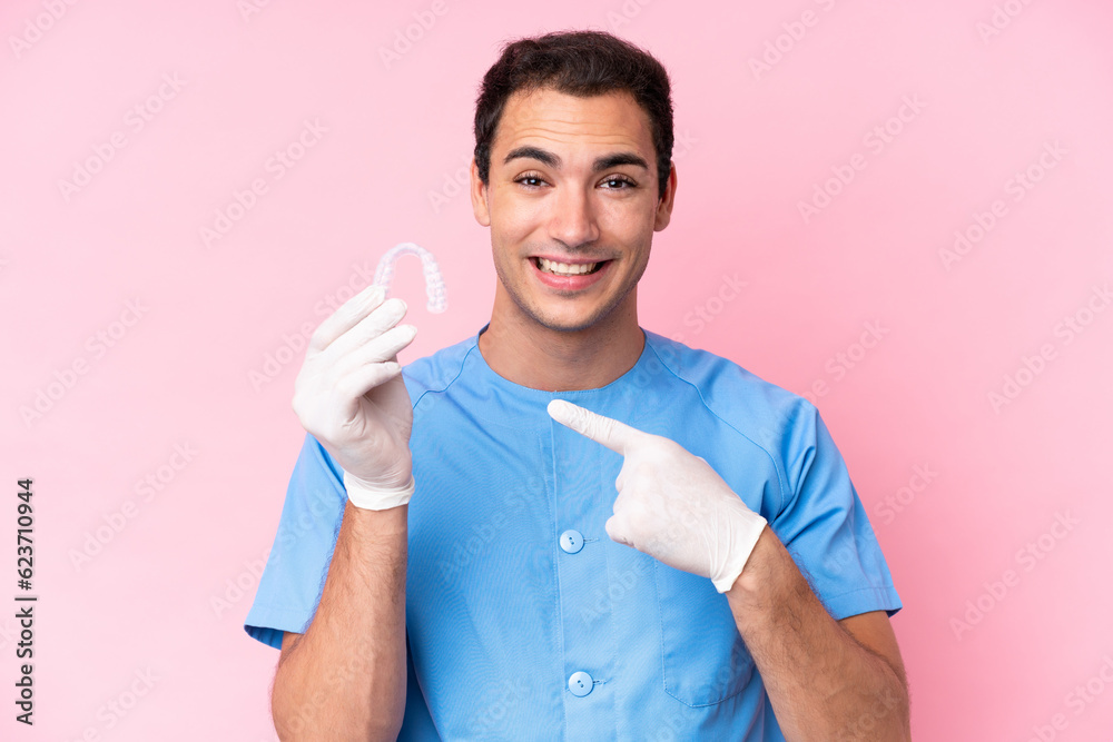 Dentist caucasian man holding invisible braces isolated on pink background pointing to the side to present a product Dentist caucasian man holding invisible braces isolated on pink background pointing to the side to present a product