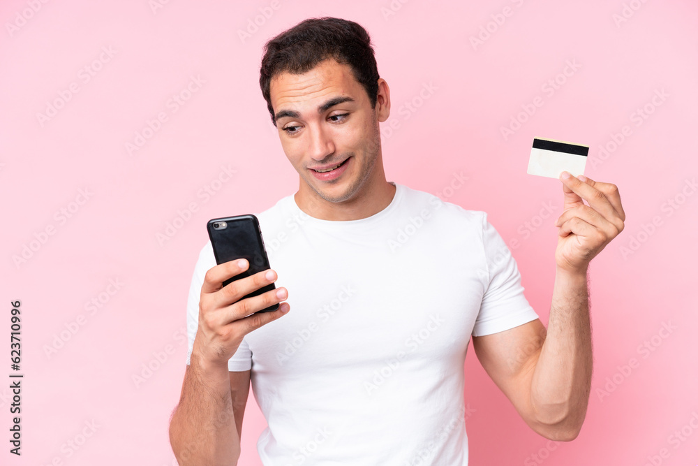 Young caucasian man isolated on pink background buying with the mobile with a credit card Young caucasian man isolated on pink background buying with the mobile with a credit card