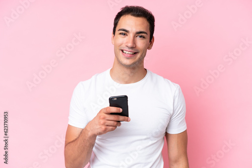 Young caucasian man isolated on pink background using mobile phone © luismolinero