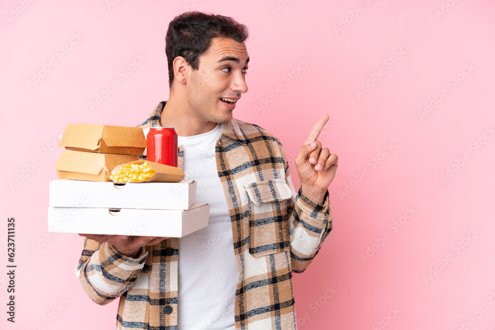 Young caucasian man holding fast food isolated on pink background intending to realizes the solution while lifting a finger up Young caucasian man holding fast food isolated on pink background intending to realizes the solution while lifting a finger up