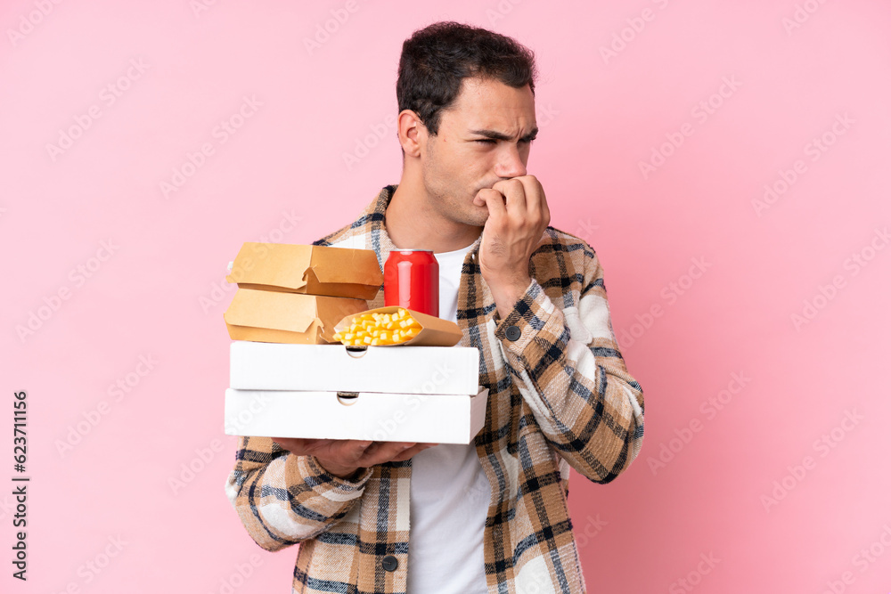 Young caucasian man holding fast food isolated on pink background having doubts Young caucasian man holding fast food isolated on pink background having doubts