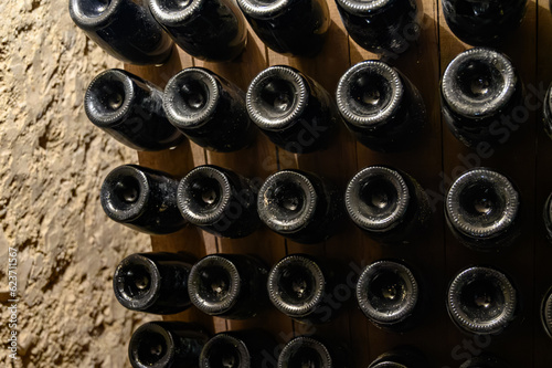 Walking in deep undergrounds caves with bottles on wooden racks, making champagne sparkling wine from chardonnay and pinor noir grapes in Epernay, Champagne, France photo