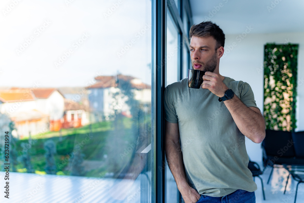 A man is drinking his morning coffee leaning against the window, his hand is in his pocket and he is thinking about new ideas Man taking a break from work and drinking coffee A man is drinking his morning coffee leaning against the window, his hand is in his pocket and he is thinking about new ideas Man taking a break from work and drinking coffee