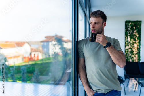 A man is drinking his morning coffee leaning against the window, his hand is in his pocket and he is thinking about new ideas Man taking a break from work and drinking coffee © DusanJelicic