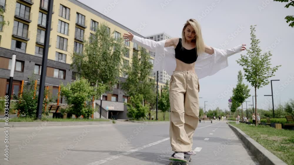 A girl is learning to ride a skateboard. Summer weather. A residential complex for a family against the background of a girl. A girl is learning to ride a skateboard. Summer weather. A residential complex for a family against the background of a girl.