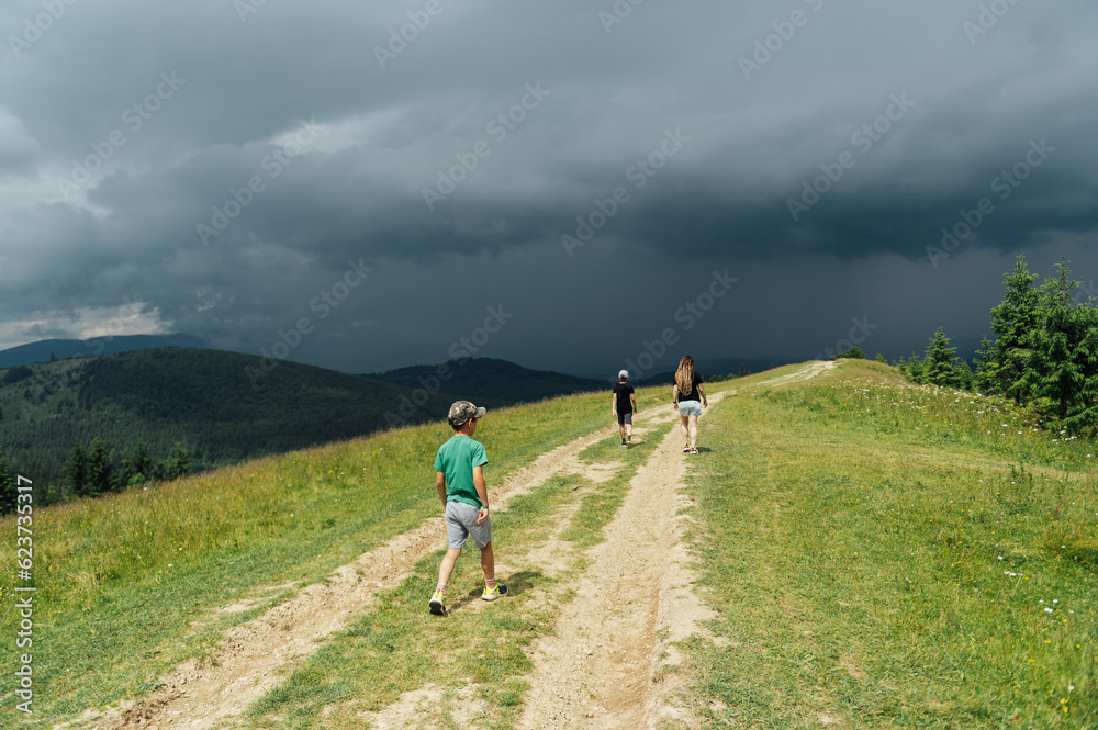 Mom with children walks in the mountains on the eve of a thunderstorm. People go down from the mountain to a safe place