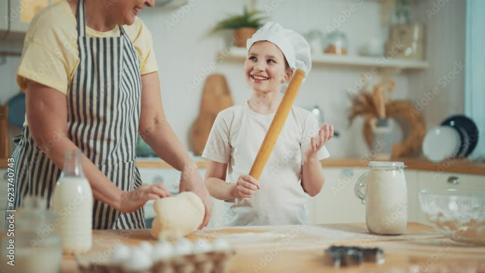 Happy granny explaining granddaughter knead dough in kitchen at home