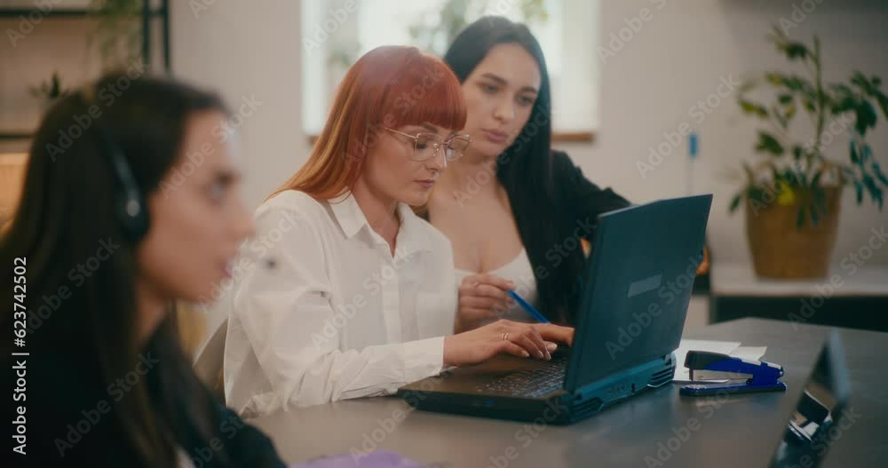 Coworkers working on laptop at desk in office.