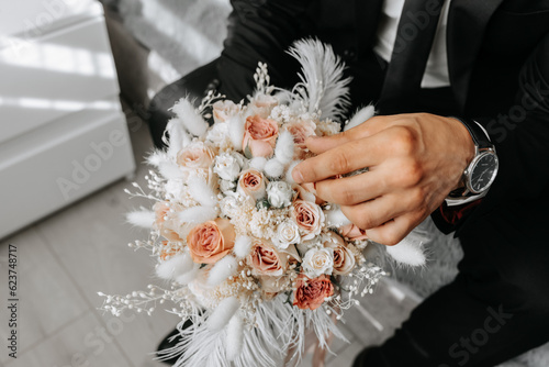 wedding bouquet of pink roses, feathers and dried flowers in the hands of the groom, close-up