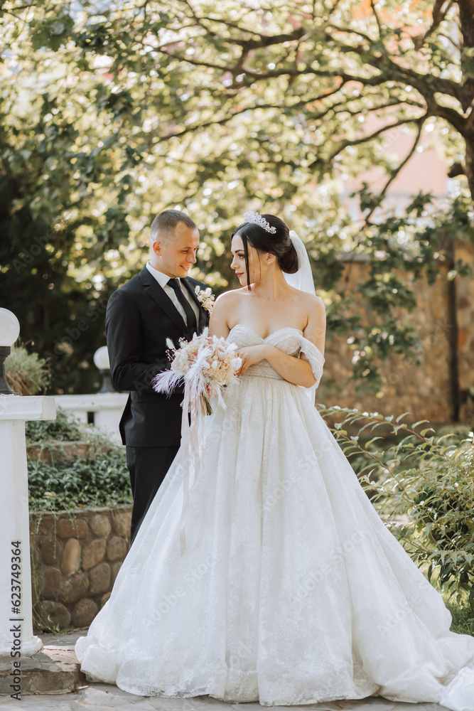 European wedding couple in the park. The bride in a beautiful dress with a long train and sleeves. Groom in a classic suit