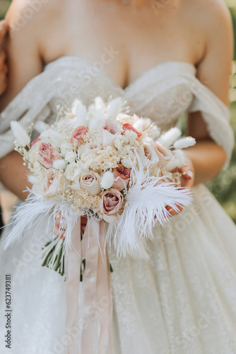 wedding bouquet of pink roses, feathers and dried flowers in the hands of the bride, close-up