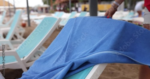 Woman hands put blue towel on sun lounger on beach. Relax on sun lounger and take seat on beach