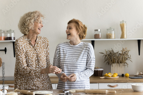 Fotografiet Joyful excited mom and adult daughter baking sweet homemade pastry snacks, cooki