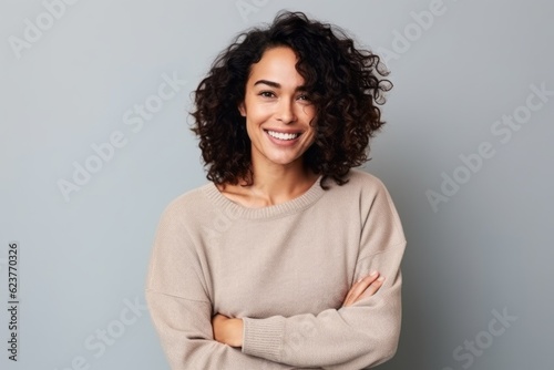 Portrait of a smiling young woman standing with arms crossed over gray background