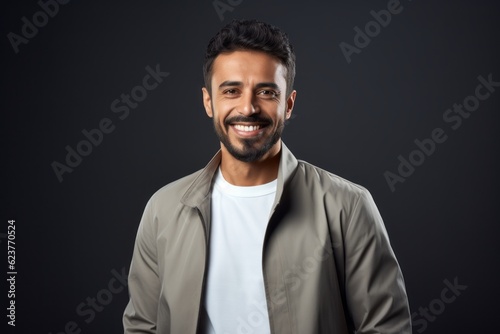 smiling young indian man in jacket looking at camera isolated on black