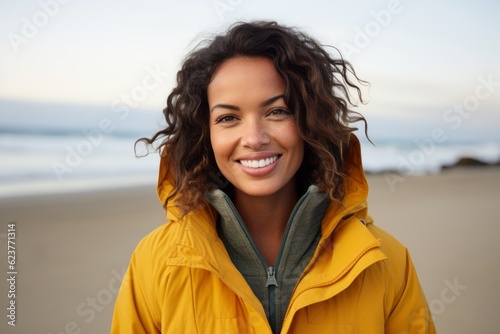 Close up portrait of a smiling young woman standing on the beach looking at camera