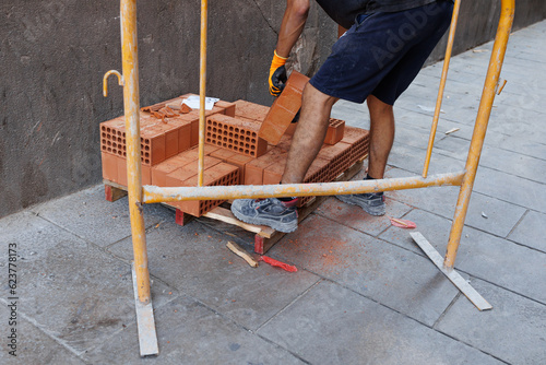 Barcelona, Spain - 2 august 2022: Construction Work - Mason Lifting a Heavy Red Brick with Gloves