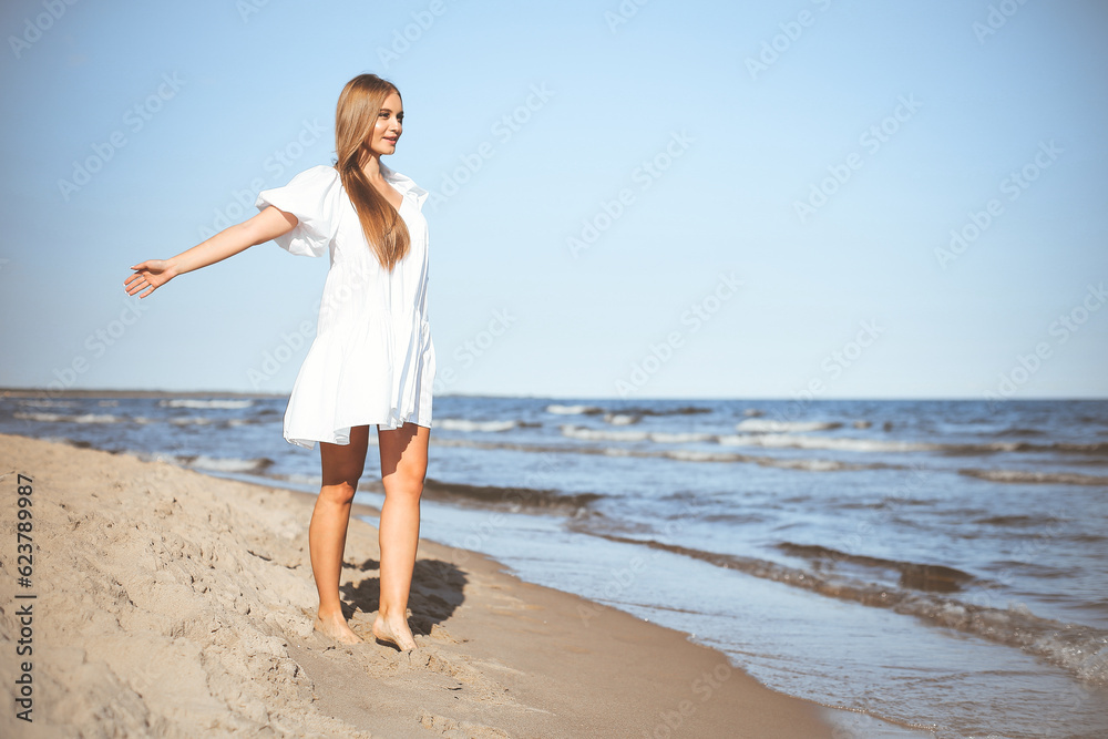 Happy smiling beautiful woman is walking on the ocean beach with open arms