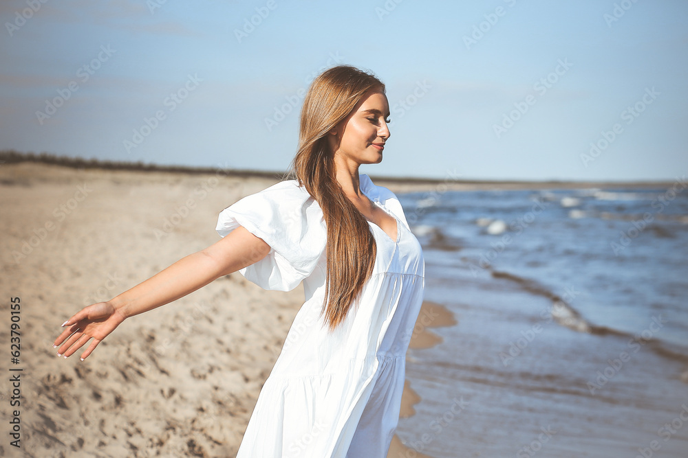 Happy smiling beautiful woman is on the ocean beach in a white summer dress, open arms Happy smiling beautiful woman is on the ocean beach in a white summer dress, open arms