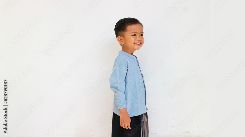 A cute and happy little boy with blue shirt and sarong looking at something A cute and happy little boy with blue shirt and sarong looking at something