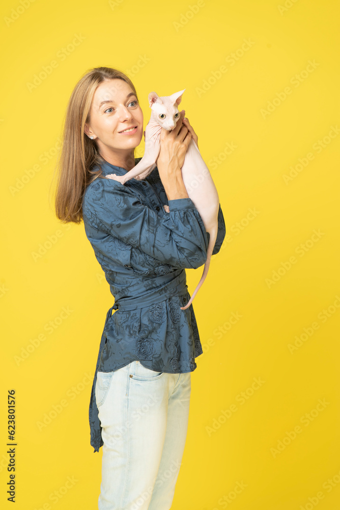 Profile of young and pretty beautiful woman posing and holding sphynx cat in hands on yellow background Profile of young and pretty beautiful woman posing and holding sphynx cat in hands on yellow background