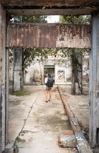 traveling girl in white shirt and black backpack discovering the ruins of a house