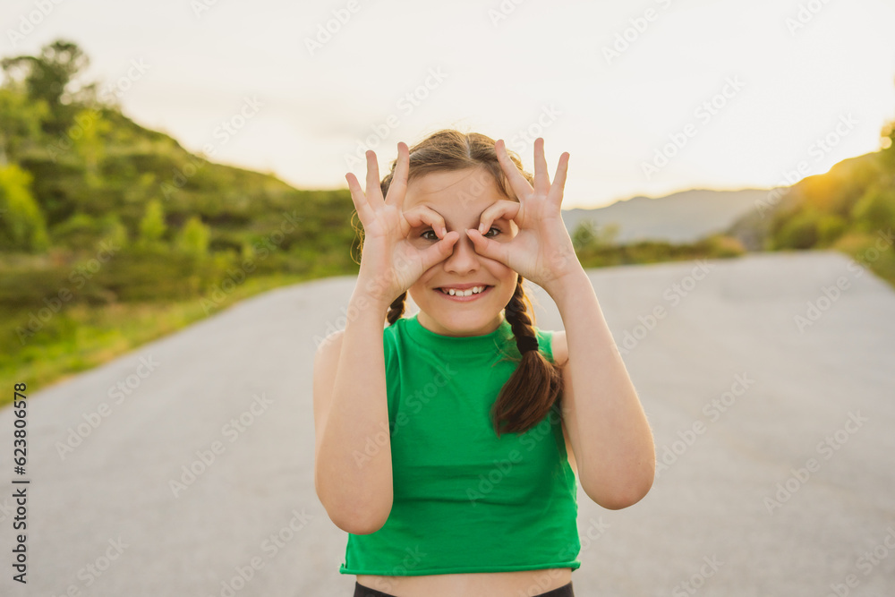 Little cute joyful girl holds her hands near her eyes in form of binoculars in nature