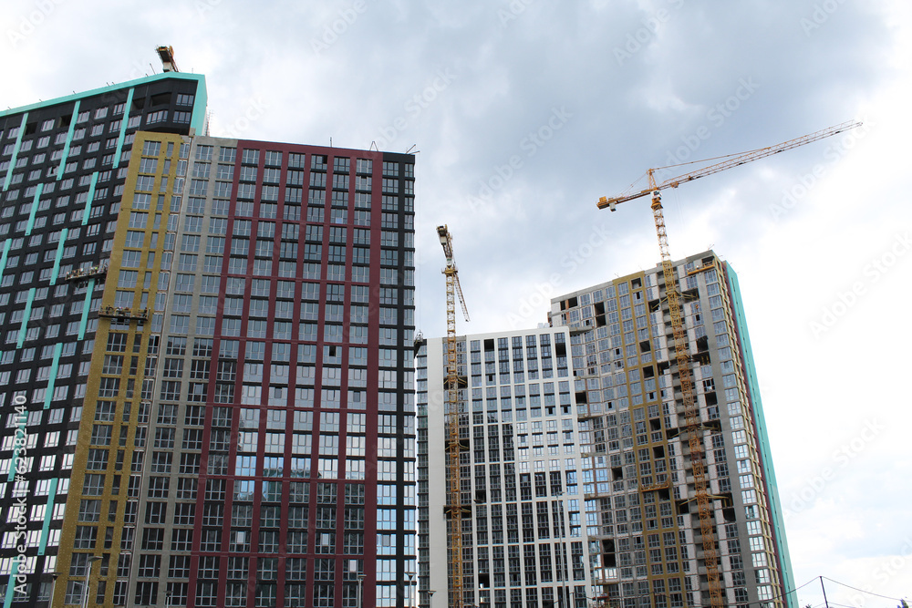 facade of a new modern building and the construction of a new building with cranes facade of a new modern building and the construction of a new building with cranes