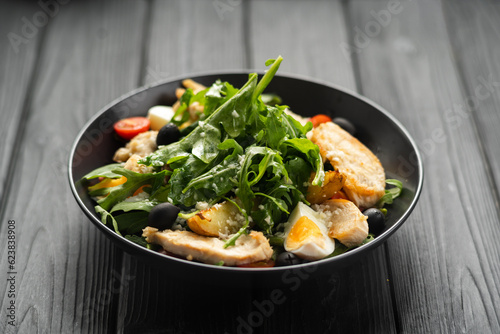 Caesar salad with fried chicken breast  egg  arugula leaves  cherry tomatoes and olives on a dark wooden background