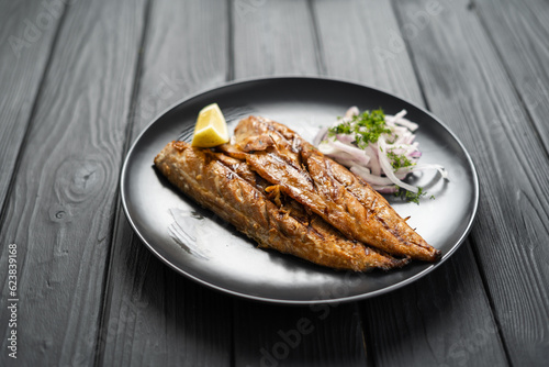 Baked mackerel fillets with lemon and onion on a black plate on dark wooden table, flat lay. Top view