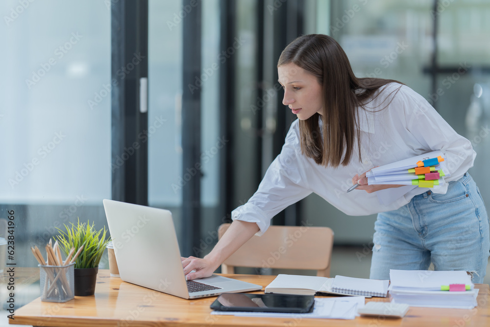 Beautiful young, concentrated businesswoman wearing shirt using smartphone while standing in modern workspace. Beautiful young, concentrated businesswoman wearing shirt using smartphone while standing in modern workspace.