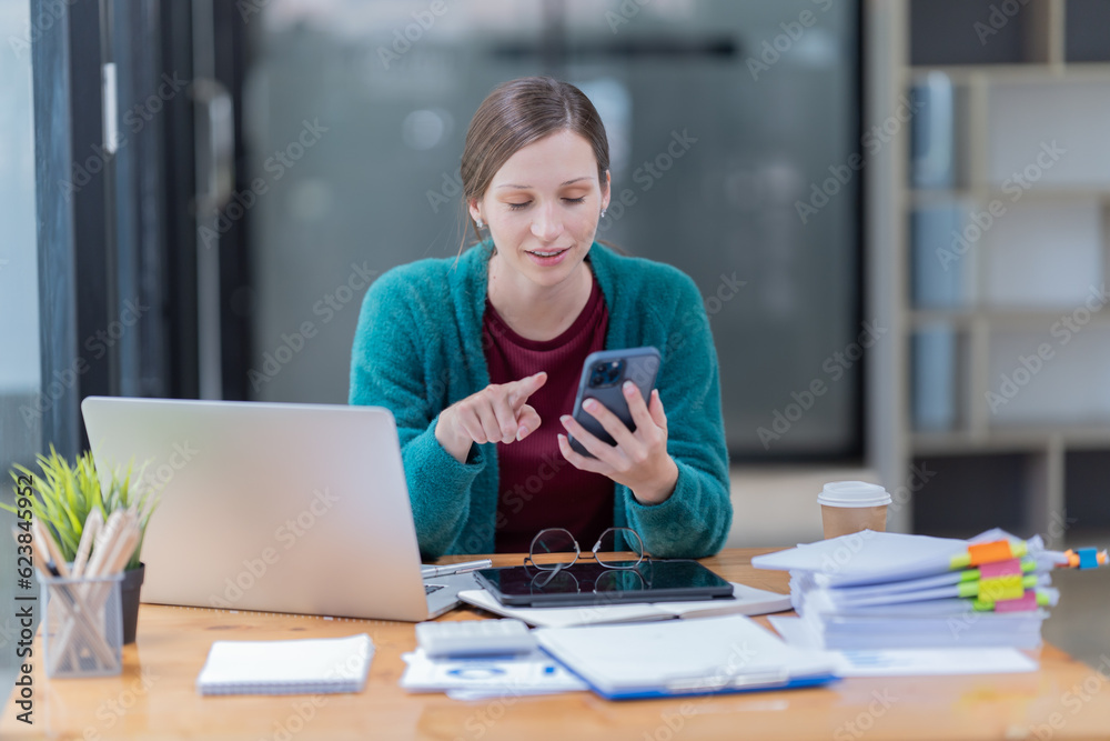 Sharing good business news. Attractive young businesswoman talking on the mobile phone and smiling while sitting at her working place in office and looking at laptop PC Sharing good business news. Attractive young businesswoman talking on the mobile phone and smiling while sitting at her working place in office and looking at laptop PC