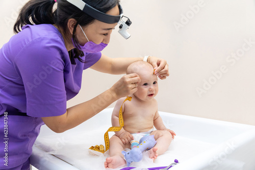medicine, healthcare and pediatrics concept - female pediatrician doctor with measure tape measuring baby girl patient's head at clinic or hospital