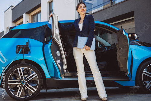 Business woman holding laptop by her electric car © Petro