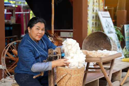 Asian woman hands picking up cotton in a bamboo basket spun by a Wooden Roller Giner. Soft and selective focus.   photo
