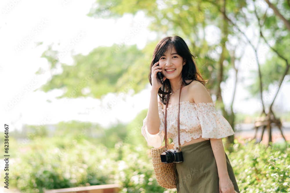 Portrait of asian young woman traveler with weaving hat, basket, mobile phone and camera on green public park background. Journey trip lifestyle, world travel explorer or Asia summer tourism concept. Portrait of asian young woman traveler with weaving hat, basket, mobile phone and camera on green public park background. Journey trip lifestyle, world travel explorer or Asia summer tourism concept.
