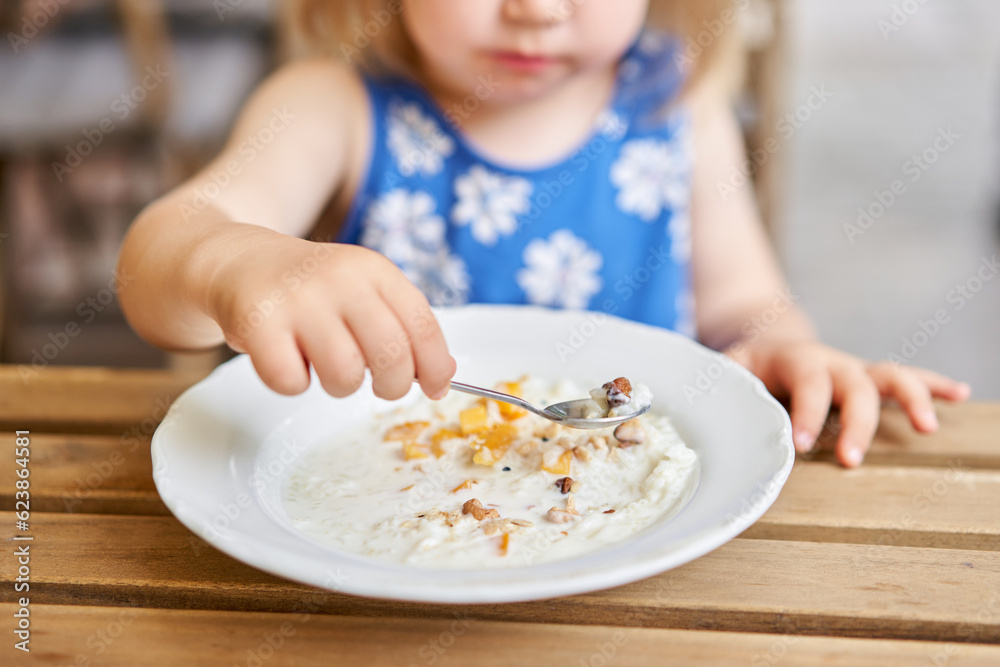 Little kid having breakfast at cafe. Adorable girl drinking still water, eating rice porridge with mango. enjoying breakfast. Little kid having breakfast at cafe. Adorable girl drinking still water, eating rice porridge with mango. enjoying breakfast.