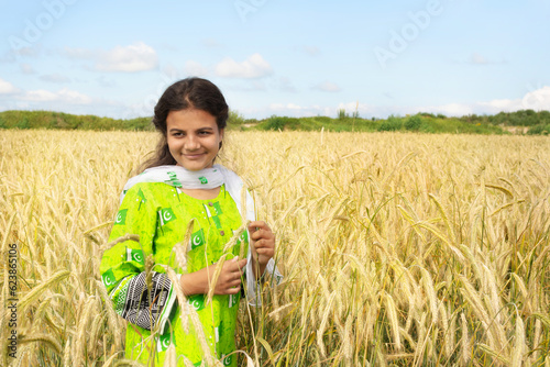 Cute pakistani girl in national dress stends in the field of golden wheat and smiling photo