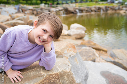 portrait of a happy boy in nature. joyful smiling, laughing teenager lies on the rocks near the mountain lake