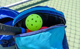 Pickleball in a sports bag with paddle. Court out of focus in background.