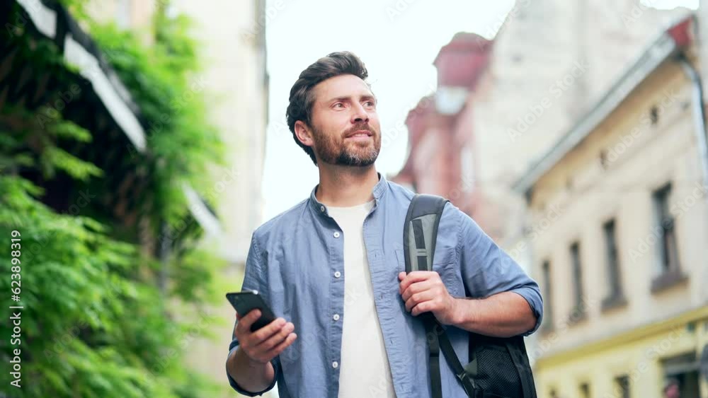 Handsome bearded man, a tourist with backpack, walk explore city street, using mobile phone. Happy male tourist traveling browsing smartphone looking at navigation app or map. Traveller lifestyle